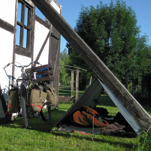 A-frame tarp tent set up behind an old house.